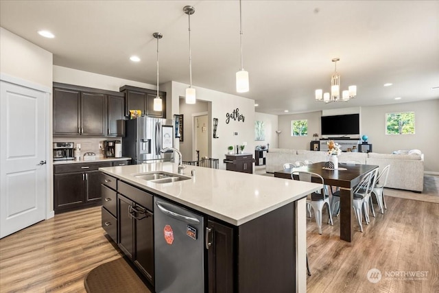 kitchen with hanging light fixtures, appliances with stainless steel finishes, sink, a center island with sink, and light hardwood / wood-style floors