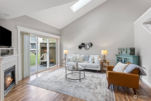 living room featuring hardwood / wood-style flooring, a tile fireplace, and vaulted ceiling with skylight