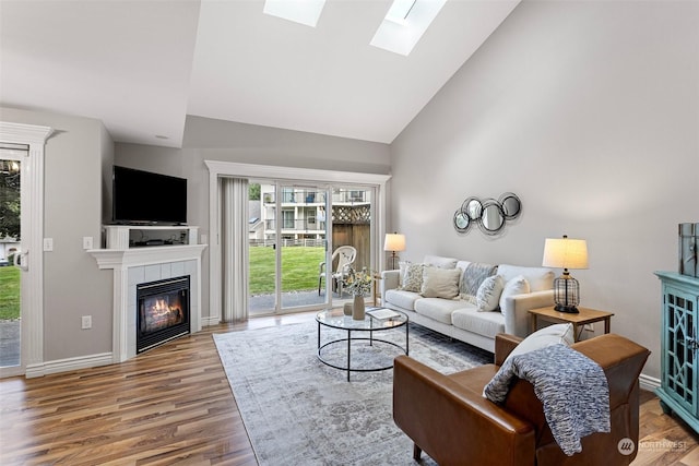 living room featuring a skylight, high vaulted ceiling, hardwood / wood-style flooring, and a tiled fireplace