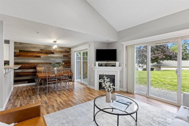 living room featuring high vaulted ceiling, light wood-type flooring, a tile fireplace, and wooden walls