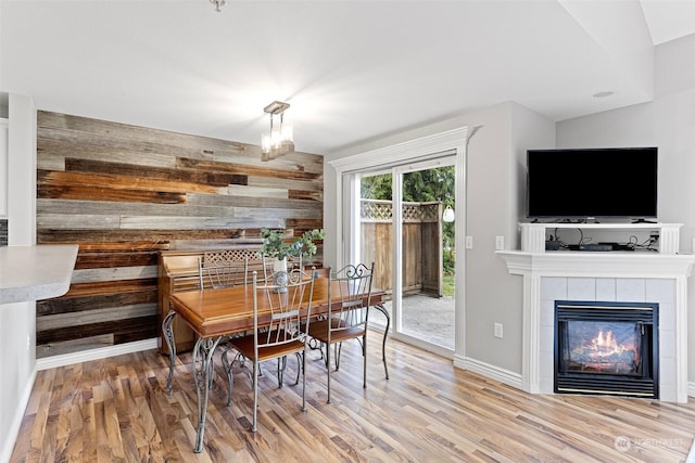 dining room with a chandelier, wooden walls, a tile fireplace, and wood-type flooring