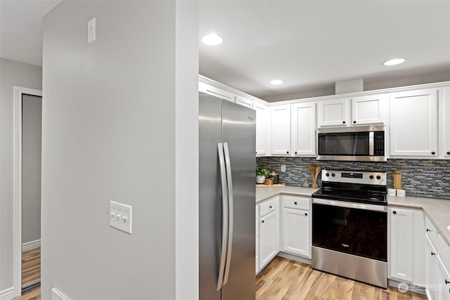 kitchen featuring backsplash, white cabinets, light wood-type flooring, and stainless steel appliances