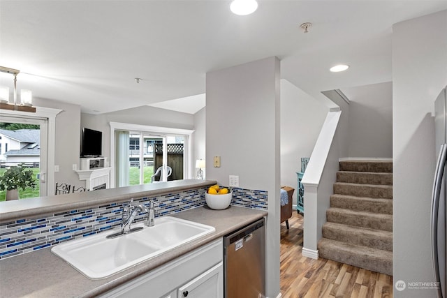 kitchen featuring stainless steel dishwasher, sink, white cabinets, light hardwood / wood-style floors, and decorative backsplash