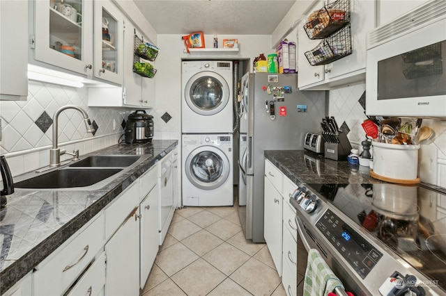 kitchen featuring appliances with stainless steel finishes, white cabinets, sink, stacked washer and clothes dryer, and light tile patterned flooring