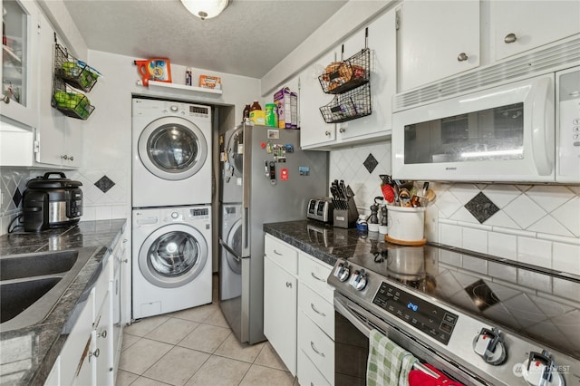 kitchen with appliances with stainless steel finishes, light tile patterned floors, white cabinets, backsplash, and stacked washing maching and dryer