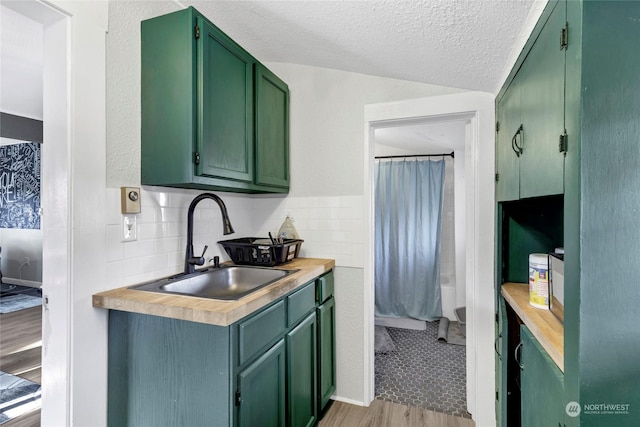 kitchen with sink, decorative backsplash, green cabinets, light hardwood / wood-style floors, and a textured ceiling