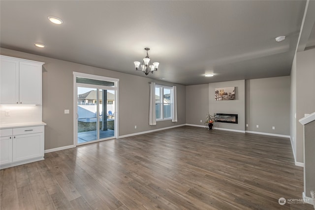 unfurnished living room featuring an inviting chandelier and dark wood-type flooring