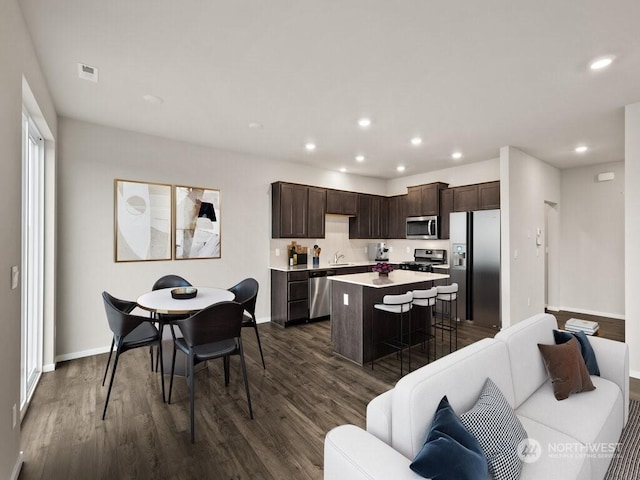 kitchen with dark brown cabinetry, a kitchen island, a kitchen bar, stainless steel appliances, and sink