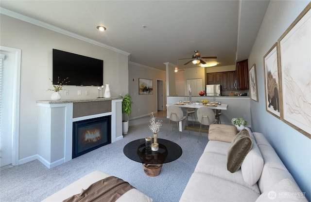 living area featuring baseboards, a glass covered fireplace, light colored carpet, and crown molding