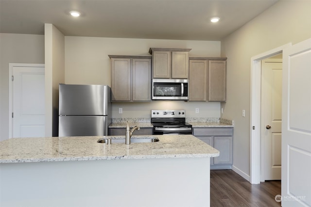 kitchen with light stone countertops, sink, an island with sink, stainless steel appliances, and dark hardwood / wood-style floors