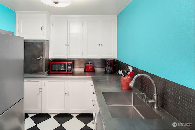 kitchen with sink, backsplash, white cabinetry, and stainless steel refrigerator