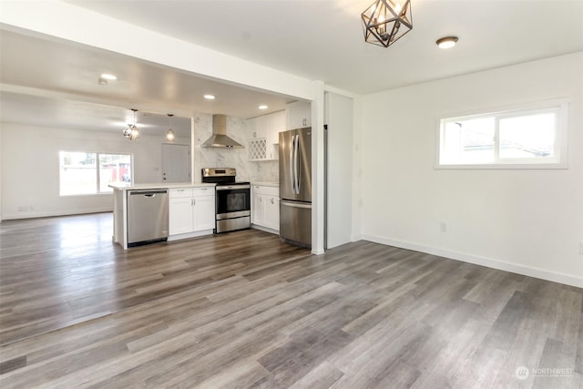 kitchen with appliances with stainless steel finishes, wall chimney exhaust hood, white cabinetry, hanging light fixtures, and kitchen peninsula