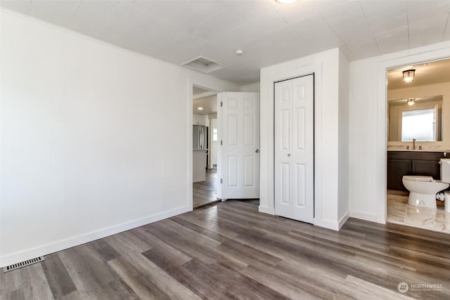 unfurnished bedroom with a closet, ensuite bathroom, dark hardwood / wood-style flooring, and sink