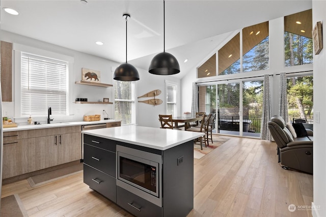 kitchen with pendant lighting, high vaulted ceiling, a center island, stainless steel microwave, and light wood-type flooring