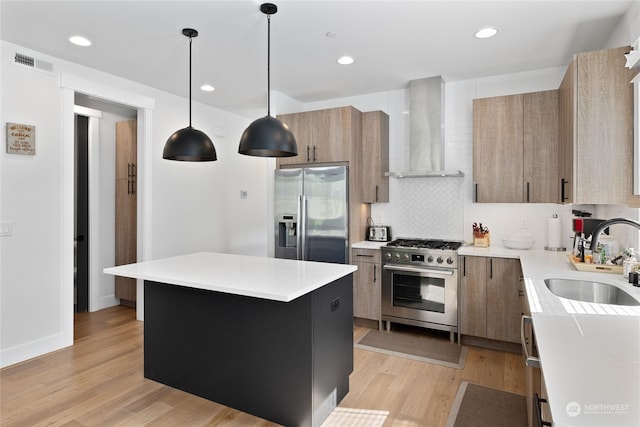 kitchen featuring appliances with stainless steel finishes, pendant lighting, sink, a center island, and wall chimney exhaust hood