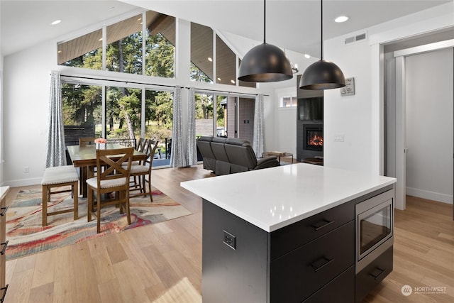 kitchen featuring light wood-type flooring, stainless steel microwave, a kitchen island, pendant lighting, and a fireplace