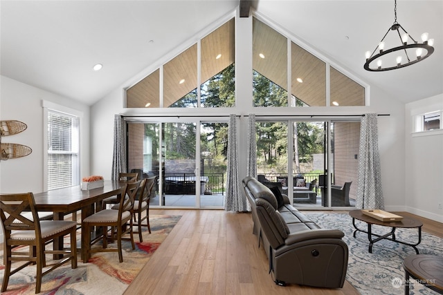 living room featuring an inviting chandelier, a towering ceiling, plenty of natural light, and light hardwood / wood-style flooring