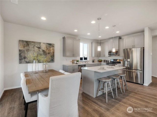 kitchen featuring a kitchen island, stainless steel appliances, hanging light fixtures, dark hardwood / wood-style floors, and gray cabinetry