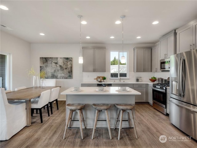 kitchen featuring stainless steel appliances, sink, hanging light fixtures, gray cabinets, and light wood-type flooring