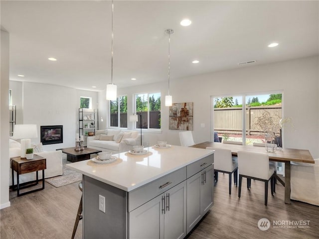 kitchen featuring a center island, gray cabinetry, light wood-type flooring, decorative light fixtures, and a breakfast bar