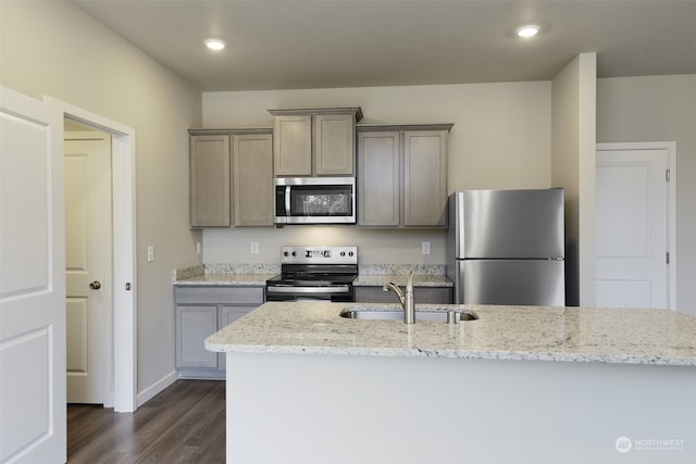 kitchen featuring appliances with stainless steel finishes, sink, dark wood-type flooring, an island with sink, and light stone counters