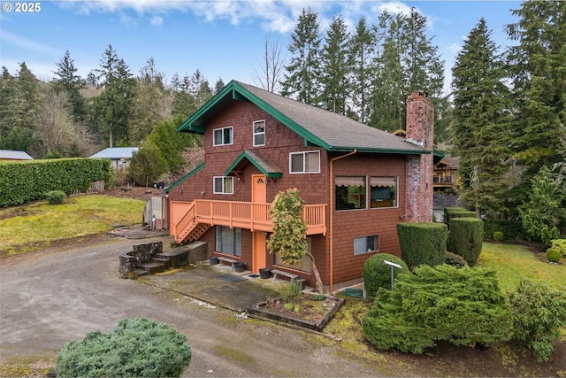 rustic home with a shingled roof, stairs, driveway, a wooden deck, and a chimney