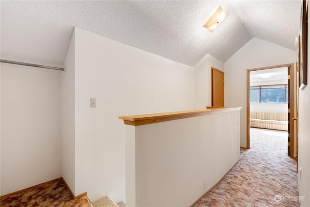 hall with light colored carpet, a textured ceiling, and vaulted ceiling