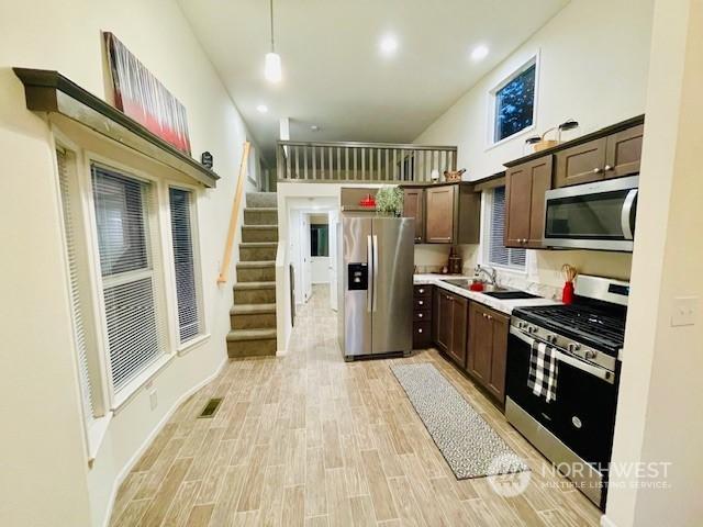 kitchen featuring decorative light fixtures, a high ceiling, light hardwood / wood-style floors, dark brown cabinetry, and stainless steel appliances