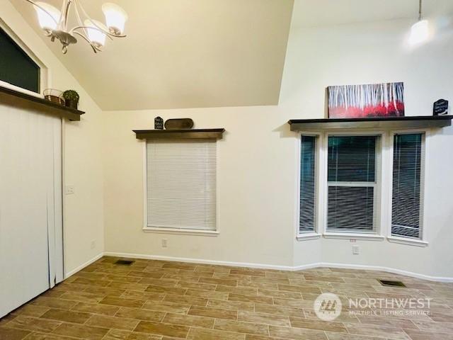 unfurnished room featuring an inviting chandelier, vaulted ceiling, and hardwood / wood-style floors