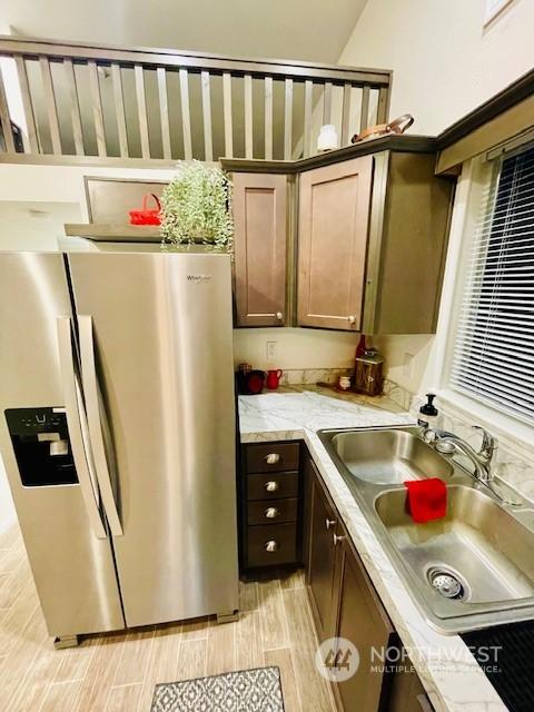 kitchen featuring light stone counters, sink, dark brown cabinets, and stainless steel refrigerator with ice dispenser