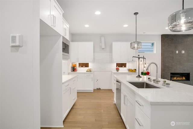 kitchen with appliances with stainless steel finishes, decorative light fixtures, sink, white cabinets, and an island with sink