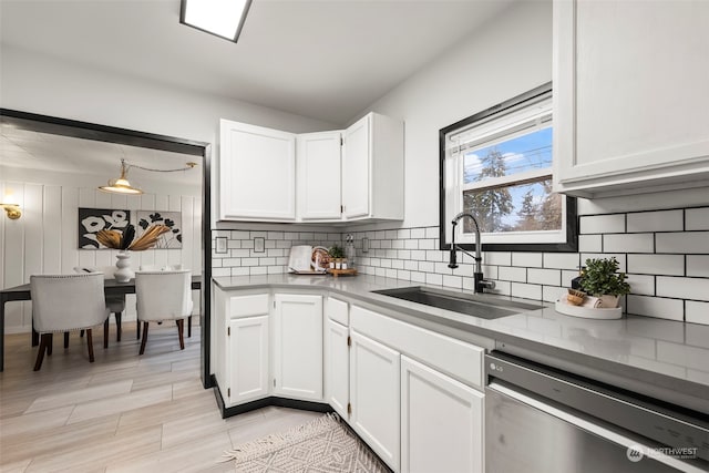 kitchen featuring decorative light fixtures, tasteful backsplash, white cabinetry, sink, and stainless steel dishwasher