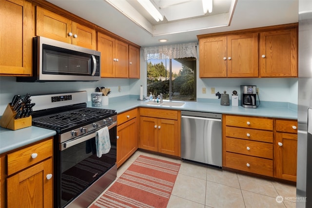 kitchen with light tile patterned flooring, stainless steel appliances, a tray ceiling, and sink