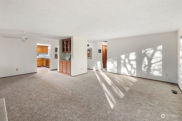 unfurnished living room featuring ceiling fan, light colored carpet, and a textured ceiling