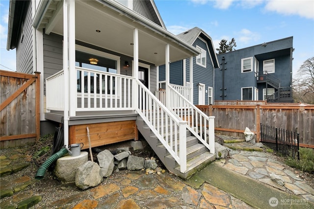 rear view of house with covered porch, stairway, and fence