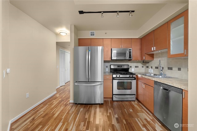 kitchen with stainless steel appliances, decorative backsplash, sink, light stone counters, and light hardwood / wood-style flooring