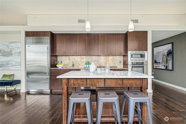 kitchen with a center island, built in appliances, tasteful backsplash, hanging light fixtures, and dark hardwood / wood-style floors