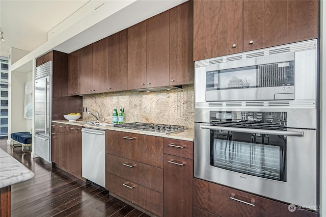 kitchen featuring built in appliances, decorative backsplash, dark brown cabinets, sink, and dark wood-type flooring