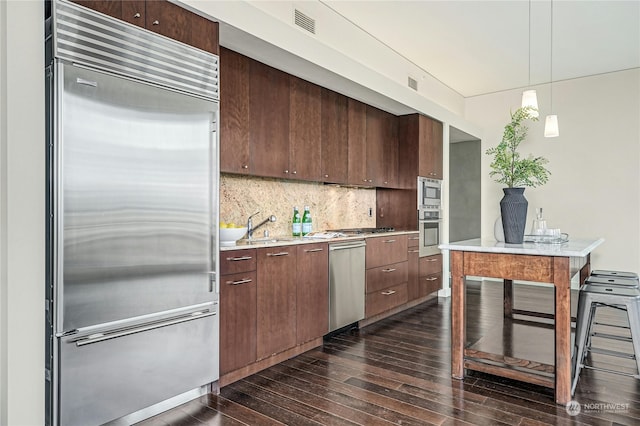 kitchen featuring dark hardwood / wood-style flooring, decorative light fixtures, sink, tasteful backsplash, and built in appliances