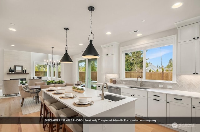 kitchen featuring sink, white cabinetry, a kitchen island with sink, and a large fireplace