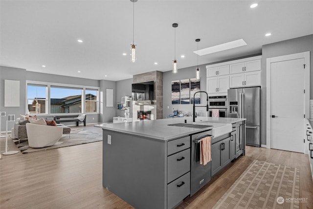 kitchen featuring white cabinetry, appliances with stainless steel finishes, decorative light fixtures, and an island with sink