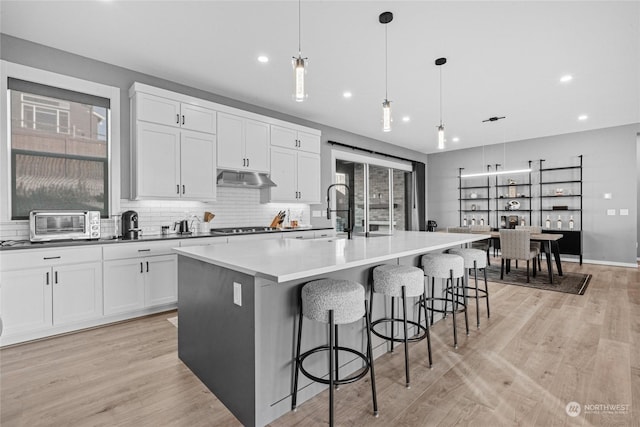 kitchen featuring hanging light fixtures, a breakfast bar area, white cabinets, and a large island with sink