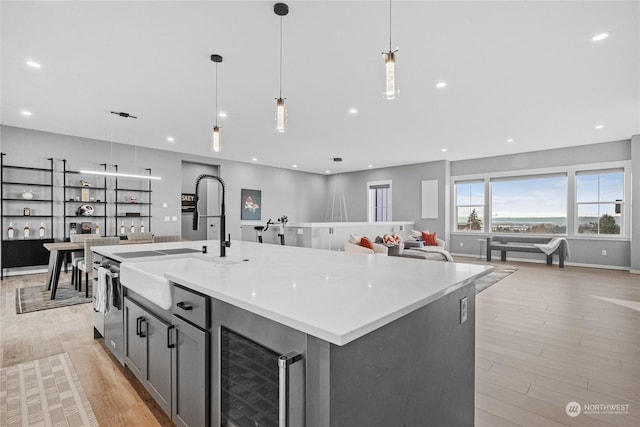 kitchen featuring sink, wine cooler, hanging light fixtures, a kitchen island with sink, and light hardwood / wood-style floors