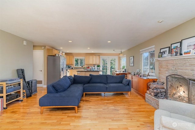 living room featuring french doors, a stone fireplace, a wealth of natural light, and light hardwood / wood-style flooring