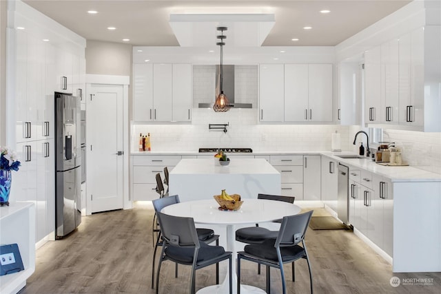 kitchen featuring pendant lighting, wall chimney range hood, sink, appliances with stainless steel finishes, and white cabinets