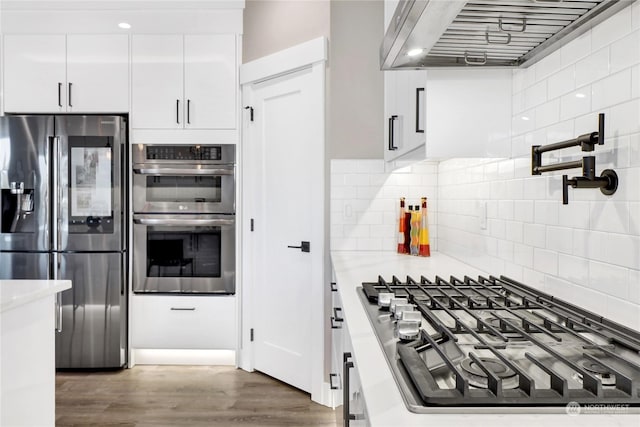 kitchen with premium range hood, dark wood-type flooring, appliances with stainless steel finishes, decorative backsplash, and white cabinets