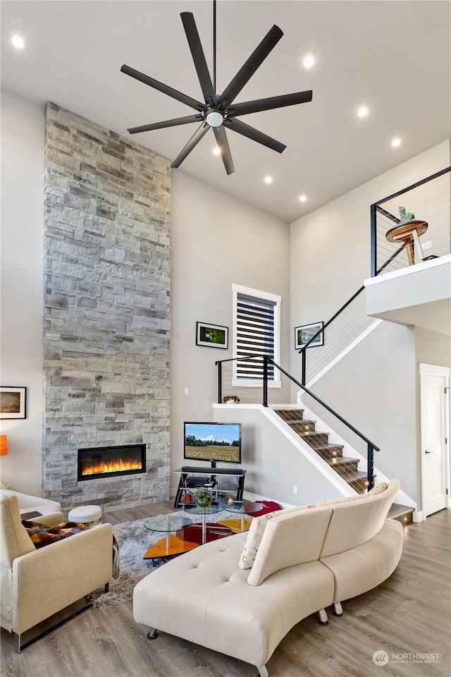 living room with ceiling fan, a towering ceiling, a stone fireplace, and light hardwood / wood-style flooring