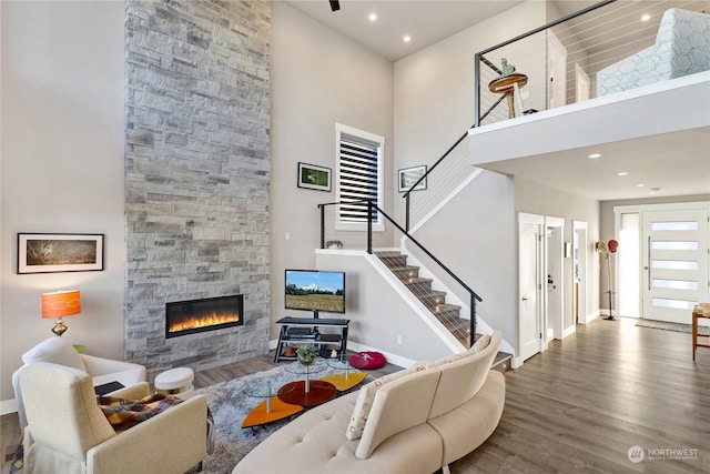 living room with a high ceiling, a stone fireplace, and hardwood / wood-style flooring