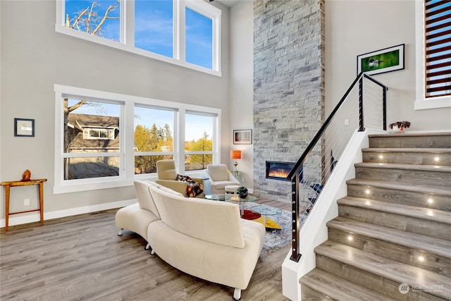 living room featuring hardwood / wood-style floors, a stone fireplace, and a towering ceiling