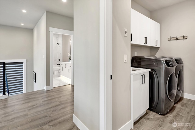 laundry room featuring cabinets, light wood-type flooring, and washer and clothes dryer